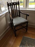 Full view of antique Victorian armchair in window corner showing dark wood finish, arms, and light-colored recovered seat.