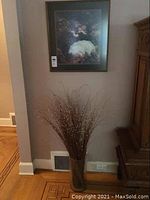 Full view of glass vase with decorative branches next to the framed print hung on wall