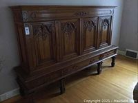 Full front view of two-piece cabinet showing four carved panels, lower drawer and bracket legs.
