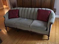 Full view of vintage three-seater sofa with beige upholstery and burgundy pillows.