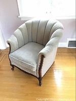 Vintage upholstered armchair with scalloped backrest and curved wooden arms shown from front angle on hardwood floor.