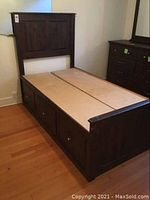 Full view of the dark stained wooden captain's bed showing the six drawers underneath and paneled headboard.