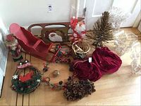 Overview of all Christmas decor items together including sleigh, nutcracker, wreath, Santa figure, pinecone clusters, red velvet bags, and faux pine trees.