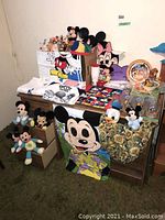 Wide view showing Disney plush props, apparel, and assorted collectibles arranged on a wooden desk and chair with a green carpeted floor.