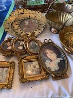 Various metal and brass decorative items shown on a table including oval and rectangular vintage-style picture frames with portrait prints and a large decorative tray with handle (14x9.5 inches).