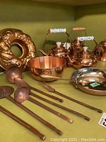Photo showing copper ring-shaped mold, two tea kettles with ceramic handles, copper bowl, small pan, and seven copper utensils laid out