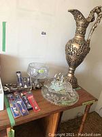 Collector spoons in packages, large glass serving platters, decorative pitcher, glass salt and pepper holders and cut glass bowl on wood shelf