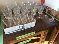 Photo showing assorted cut glass and lead crystal glassware arranged on a wooden surface, some in a box, with various sizes and styles visible.