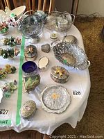 Overview of various silver plated jewelry boxes, glass crystal dishes, and decorative items on a white tablecloth.