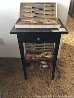 Full view of all bone handle steak and carving cutting tool sets displayed on black wooden side table with drawer, arranged in open boxes showing knives and forks.