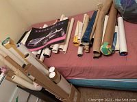 Photo showing multiple rolled posters in cardboard tubes and some flat posters on bed including a Lotus car poster.