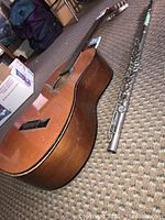Acoustic guitar and silver metal bass flute on carpet