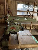 Full shot of green DeWalt radial arm saw mounted on wooden table showing saw blade, arm with DeWalt logo, and base.