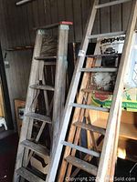 Three wooden ladders of varying sizes and styles, against wall, showing condition and details