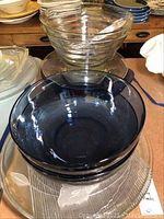 Several assorted glass serving bowls stacked, varying in size and color including clear ribbed and blue tinted glass bowls