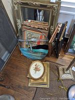 Wide shot showing pile of artwork and mirror on floor with visible stained glass, frames, needlepoint and mirror.