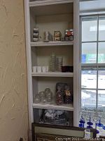 Shelving with various candle holders, votive candles, and pinecone shaped candles shown in bags and glass holders.