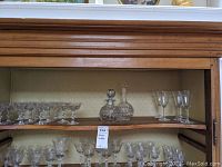 Shelf with 11 champagne glasses, 2 glass carafes with stoppers, and 4 etched wine glasses.