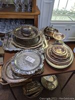 Overview of assembled silver plated trays, platters, creamer, gravy boat, sugar bowl, and compote on a table showing tarnish and wear