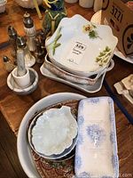 Top-down view of assorted Limoges dishes with floral decoration, salt and pepper shakers, and pestle and mortar.