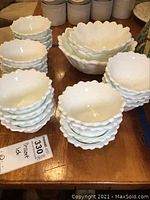 Multiple stacked small white milk glass dessert bowls and a set of three larger serving bowls on a table