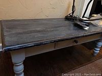 Rectangular wood coffee table with dark stained top surface and white rounded legs, showing worn condition.