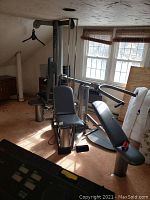 Full view of machine in attic room showing bench seat, pulleys and free weight plates