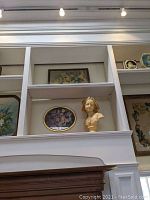 Wide view of shelves displaying the bust and oval framed floral painting together
