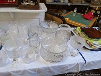Table with assorted crystal punch bowl set, serving bowls, vases, drinking glasses, and ice bucket showing starburst and cut glass patterns