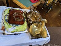 Several decorative trays including wood, plastic, and ceramic along with metal horns and a brass pumpkin on a table