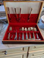 Full open wooden box with flatware arranged in slots, forks standing vertically and spoons and knives placed horizontally in the lower section.