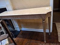 Overall view of rectangular stone top sofa table with carved wooden base under mantle and partially on rug