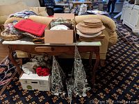 Full view of table displaying woven placemats, red paper napkins, wicker napkin holders, heart-shaped mirrors, beaded red hearts, and boxes of other small holiday decorations under table.