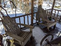 Photo showing two weathered wooden Adirondack chairs on a porch with snow and trees visible in the background.
