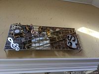 Image of large mixed media wall art sculpture featuring a trombone, musical notes, cherubs and decorative plaques mounted on a metal grid base.