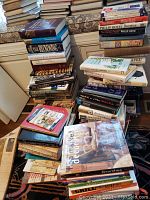 Photo of stacked books including novels, cookbooks, and hobby books with visible titles such as Philip Roth books and general cookbooks.