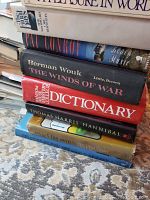 Stack of assorted books including dictionary, novels, and non-fiction, showing titles like The Winds of War and Hannibal.