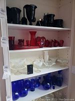 Shelves of glassware showing red glass items on middle shelf, black glass on top, white on next shelf, and blue on bottom.