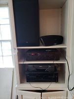 White shelving unit holding multiple audio components and speakers: ADS speaker at top left, JBL dock at top right, Yamaha receiver below, Philips VCR and Sony DVD player below that, Sony 5-disc changer at bottom.