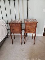 Pair of antique wooden nightstands with reddish marble tops, curved legs, and wooden knobs, placed side by side against a wall.