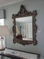 Full view of large rectangular ornate wall mirror hanging on a wall above a console table.