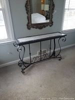 Full view of rectangular sofa table with mosaic glass top, iron frame featuring scrollwork legs, positioned against a wall under a mirror.
