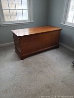 Full view of the vintage wooden chest placed in a corner of a room showing its rectangular shape and wooden finish.