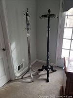 Two wooden coat racks side by side, one dark wood with traditional turned design, one silver painted with square post and multiple hooks