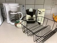 Wide shot of kitchen appliances including Rival coffee maker, Proctor Silex juicer, Kenmore can opener, filters, and black metal rack