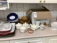 Overview of kitchenware items on a countertop showing CorningWare dishes, wooden bowls, mugs, and some baking dishes.