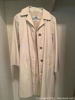 Front view of the beige Aquascutum raincoat showing collar, buttons, and sleeve length.