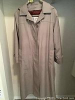 Beige long raincoat on hanger showing full front view with button closure and pocket details.