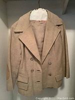 Full view of beige The Bay jacket hanging on hanger with elbow patches and flap pockets.