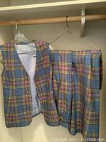 Three-piece clothing set hanging: vest, skirt, and pants in a multicolor plaid pattern.
